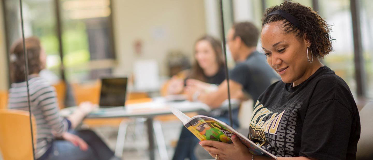 女学生穿着奥克兰大学的黑色衬衫，正在看书万博ManBetX登录