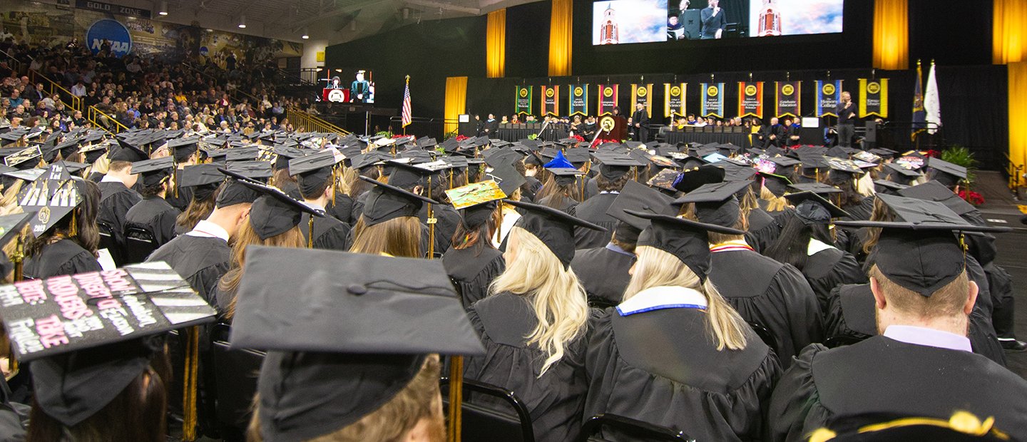毕业生们戴着帽子，穿着长袍，面对着舞台。