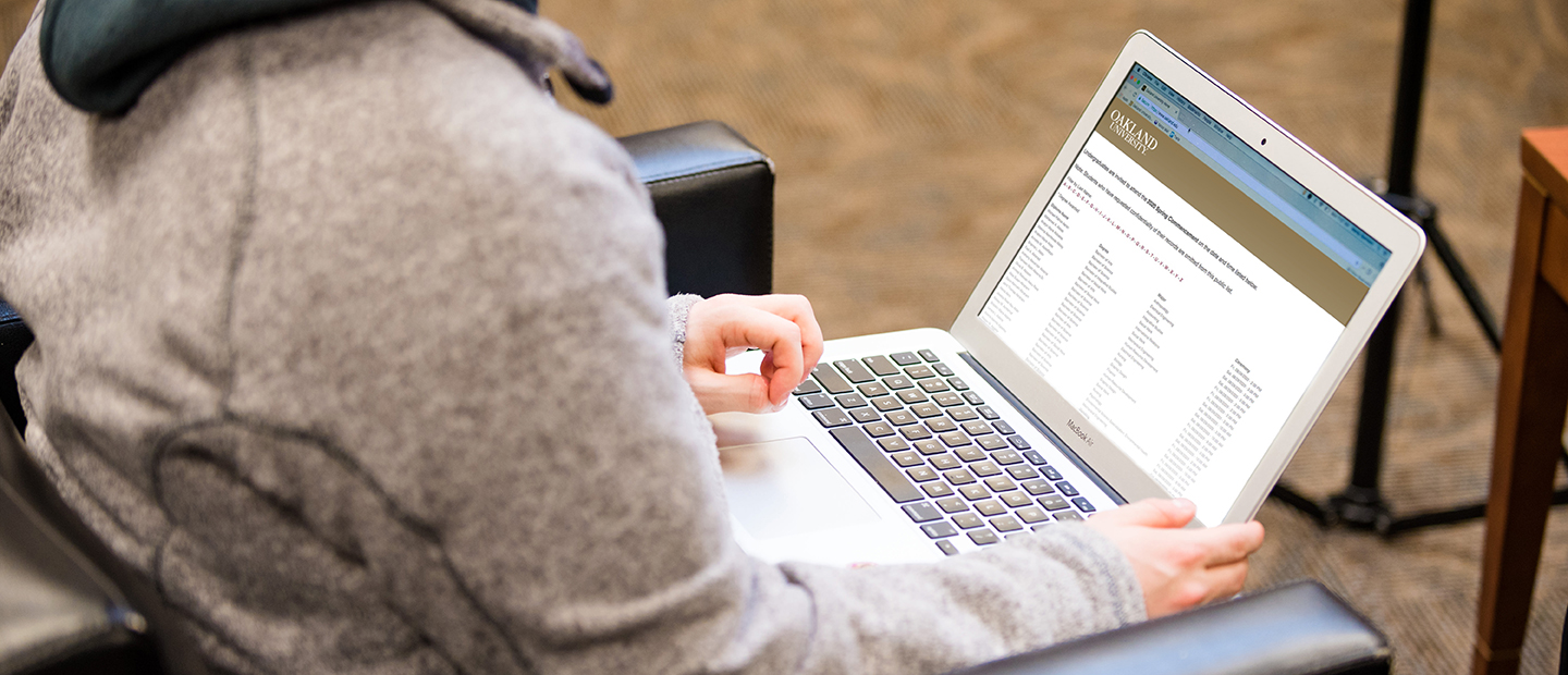 一个人坐在打开的笔记本电脑上，显示着奥克兰大学的网页。万博ManBetX登录