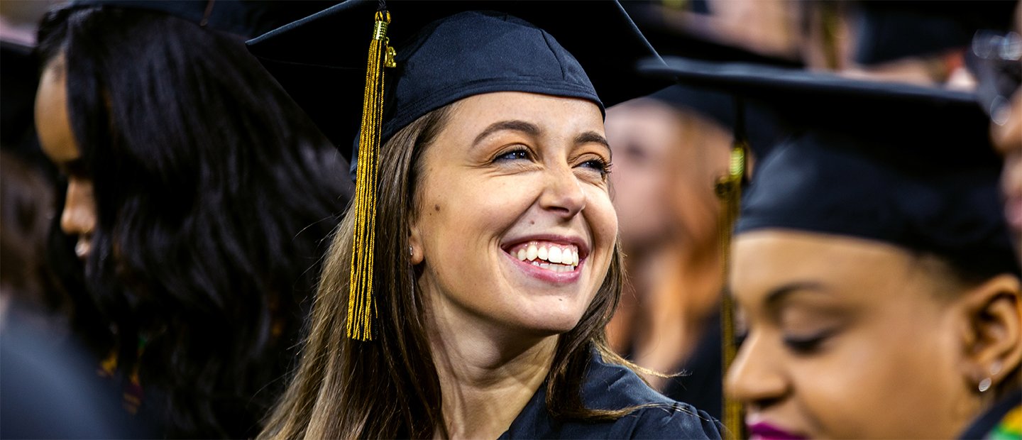 毕业典礼上，一位戴着帽子和长袍的年轻女子面带微笑。