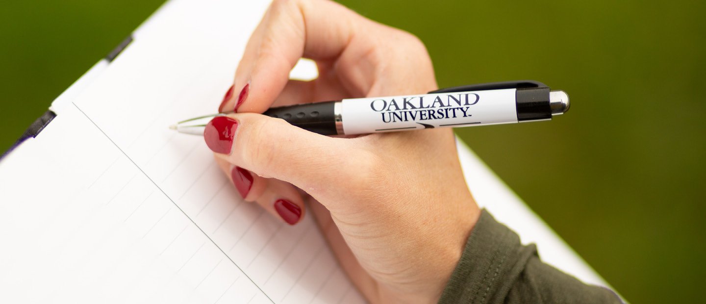 一只手拿着奥克兰大学的笔放在笔记本上万博ManBetX登录。
