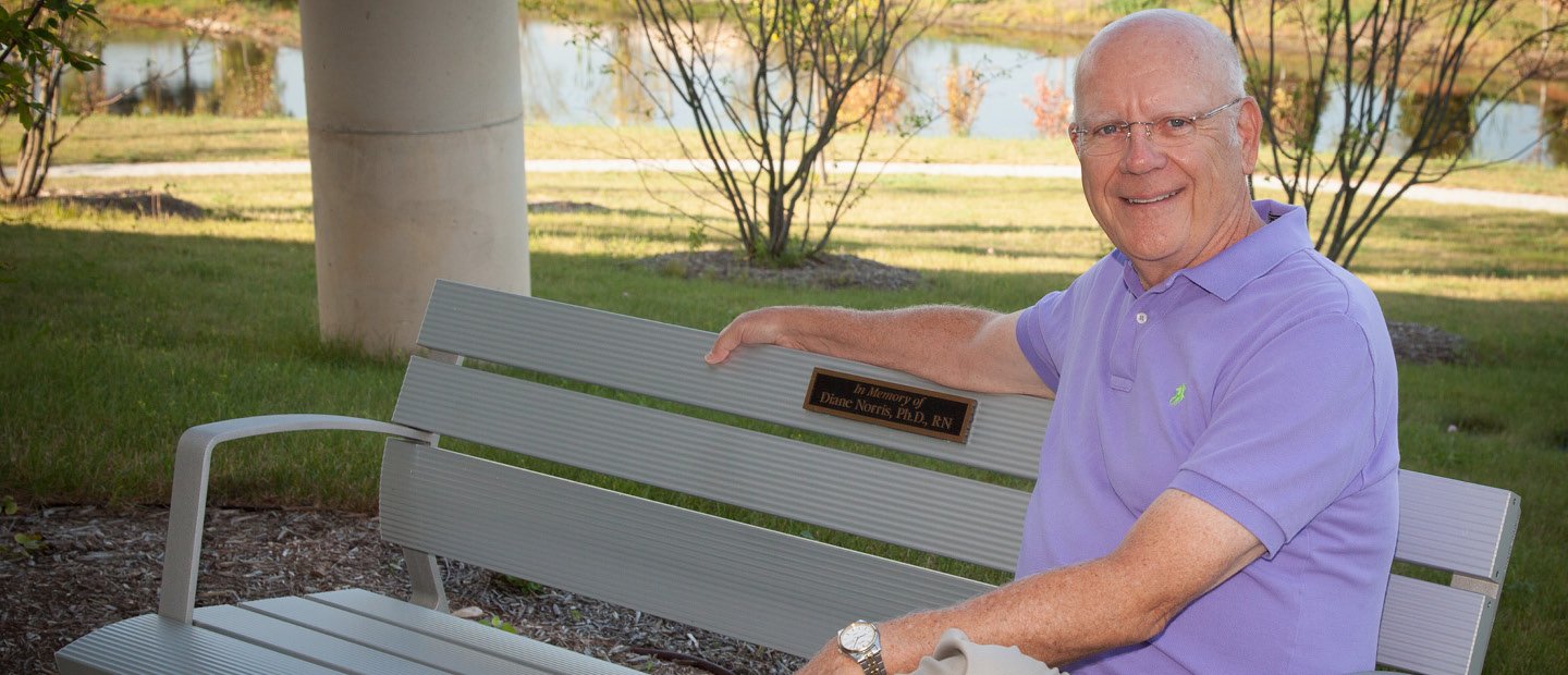 一个男人坐在长凳上，上面写着“纪念黛安·诺里斯博士，注册护士”。