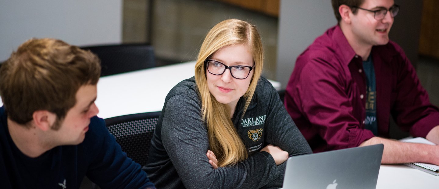 一名女学生穿着奥克兰大学的灰色衬衫，面前放着一台打开的笔记本万博ManBetX登录电脑，一名男学生坐在她的左右