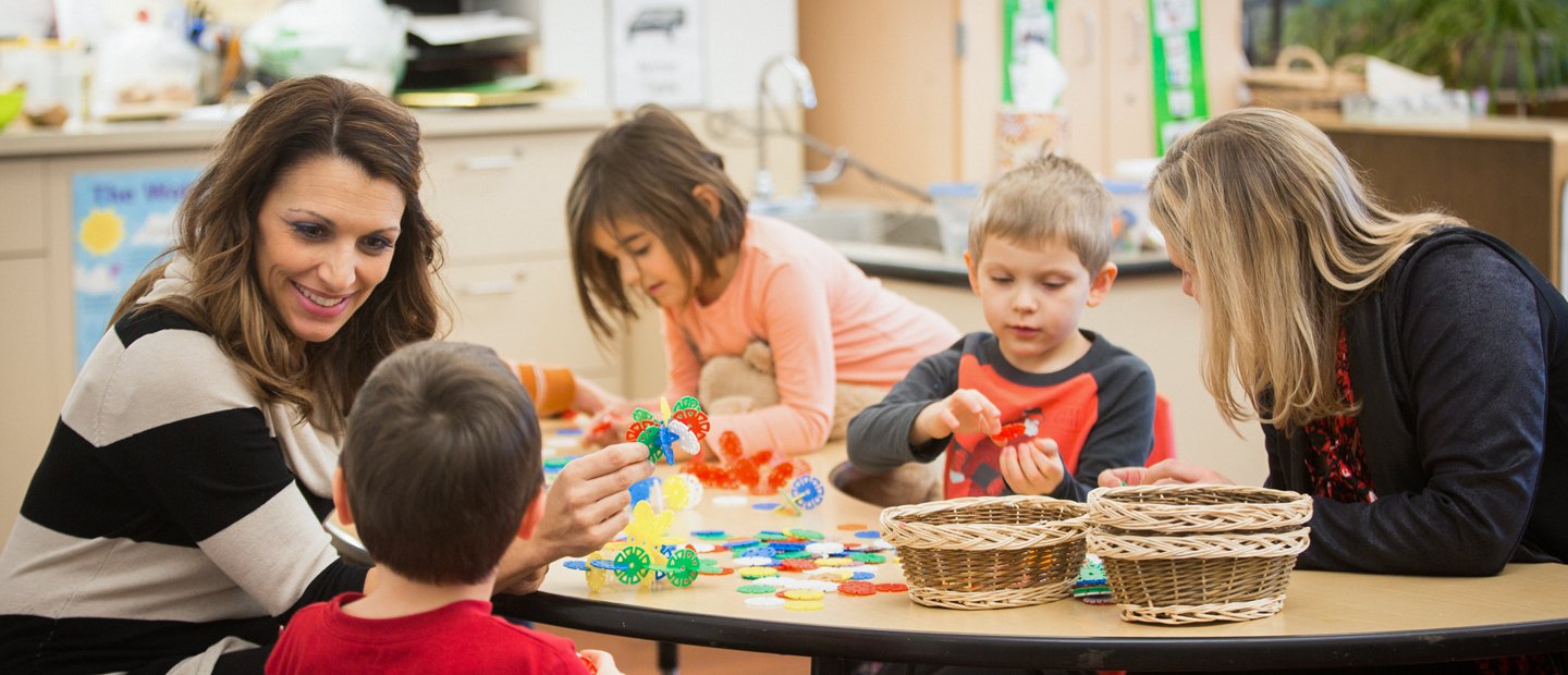 两名女教师和三名年轻学生在教室里玩五颜六色的玩具。