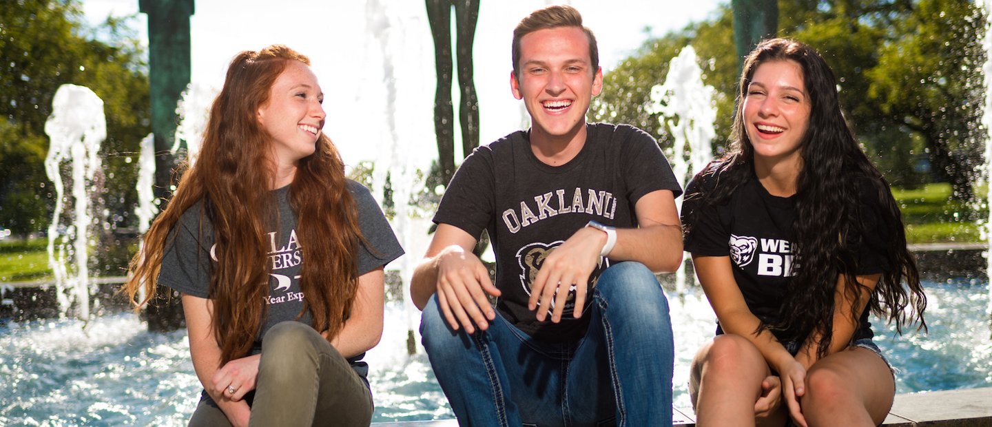 三个奥克兰大万博ManBetX登录学的学生坐在喷泉边，笑着笑着。