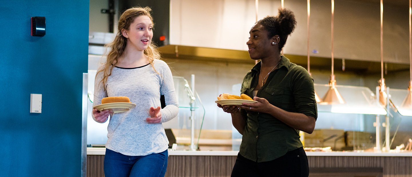 两个女学生拿着盘子的食物在餐厅