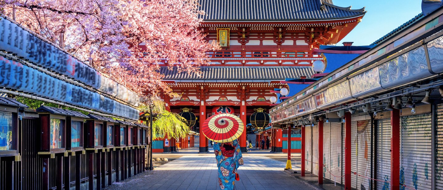 一个人拿着红白相间的雨伞，走在日本建筑物之间的小路上。