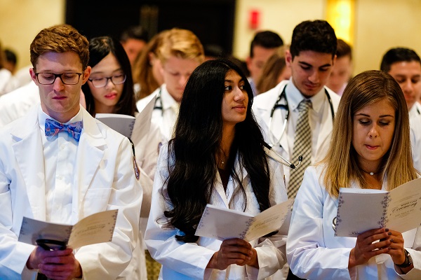 学生站起来,拿着项目,在穿白大衣的仪式。