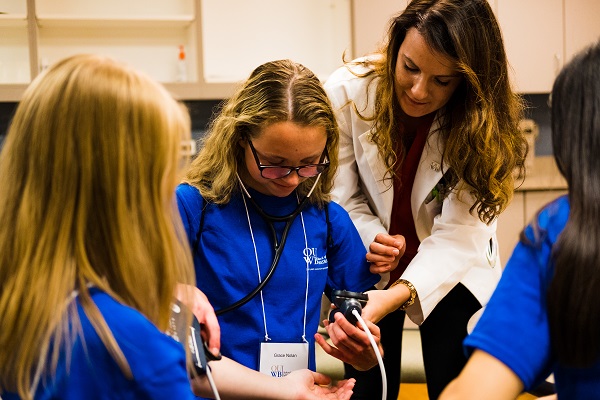 一名OUWB学生帮助一名高中生佩戴血压计。