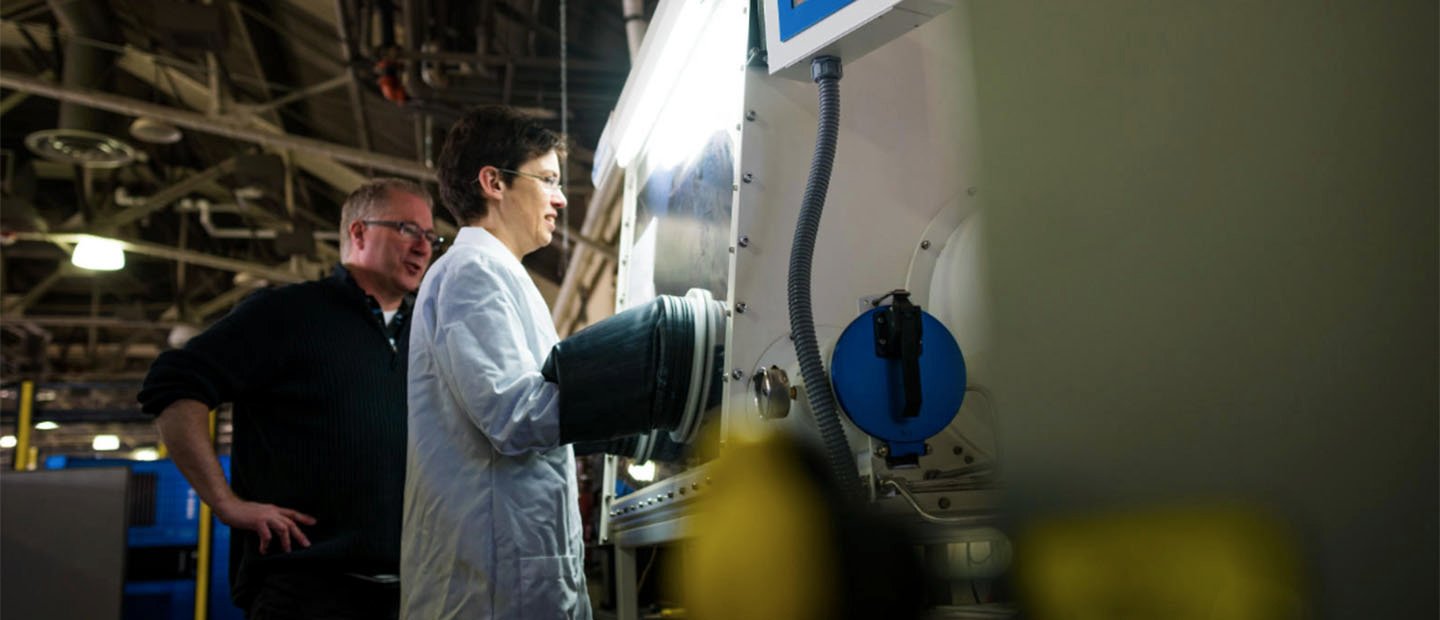 一个女人穿白大褂的工作在一家大型的机器,一个人看在她的肩膀上。