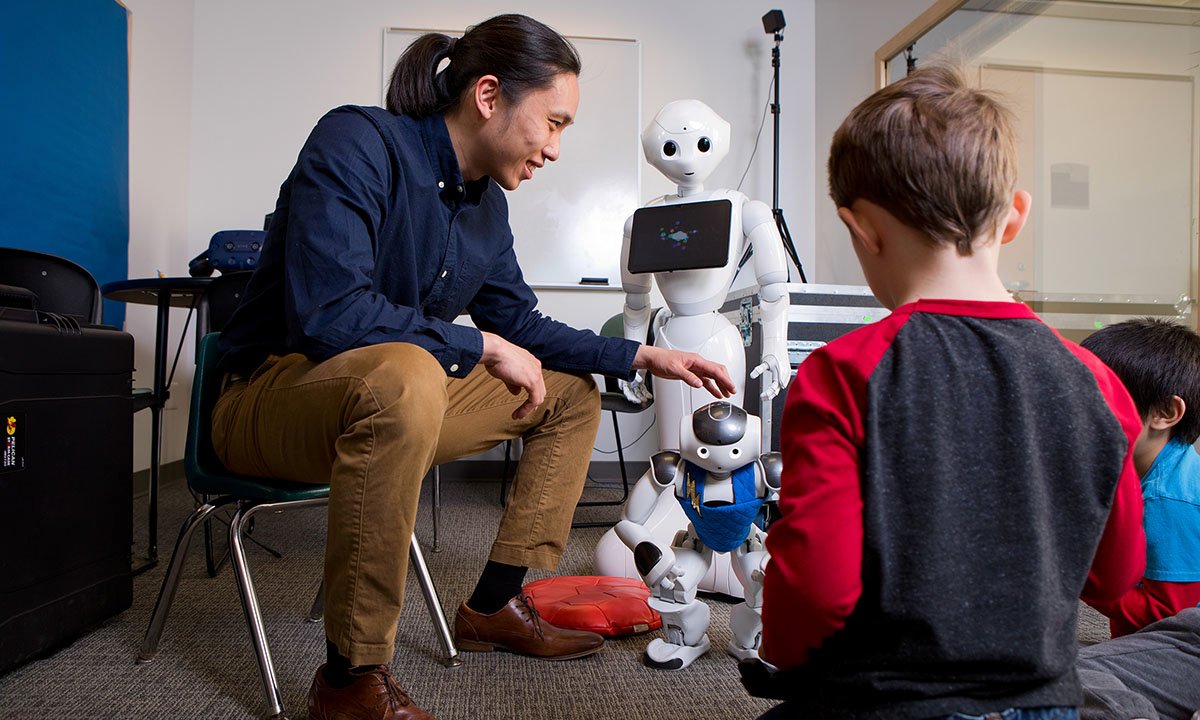 一名男子坐在椅子上向两个孩子展示机器人