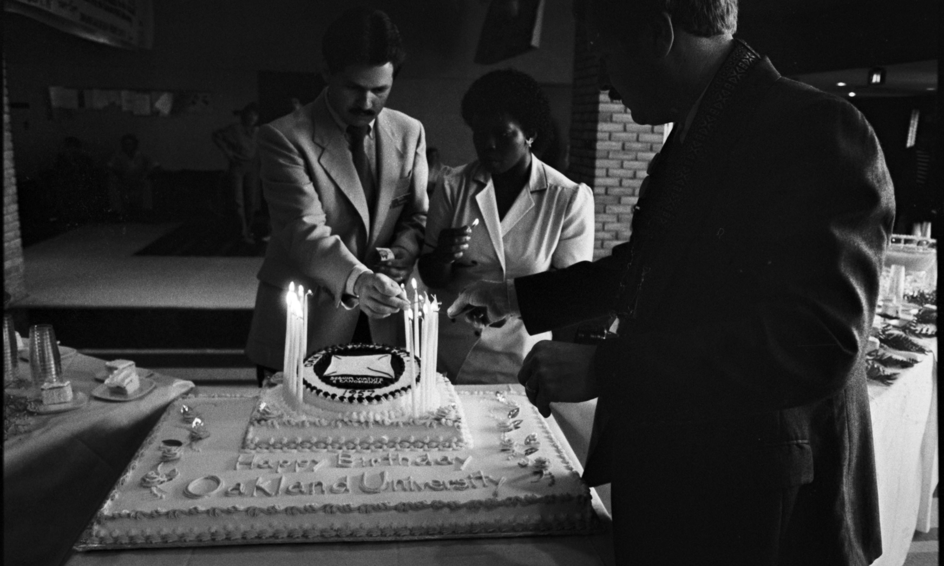 三个人点燃蛋糕，上面写着“奥克兰大学生日快乐”万博ManBetX登录