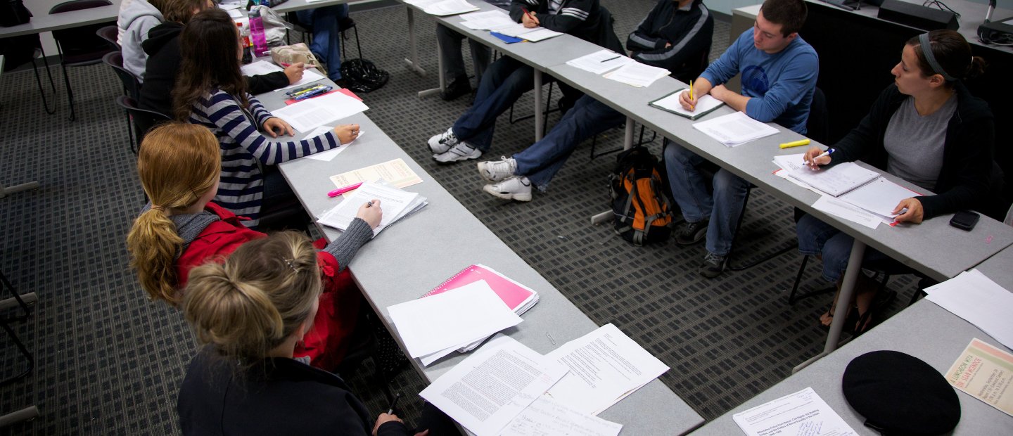 学生们坐在长方形的桌子旁，在笔记本上写字。