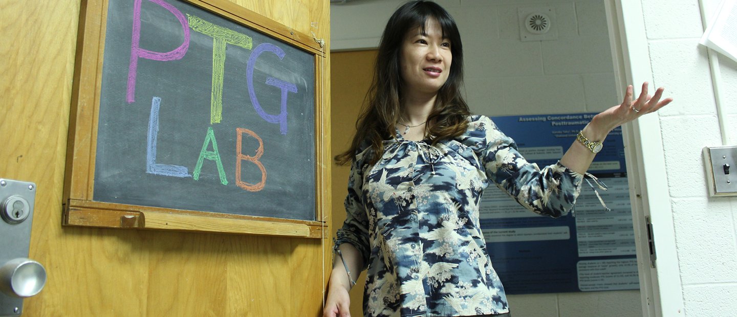 一位教授站在黑板前，黑板上写着“P T G实验室”。