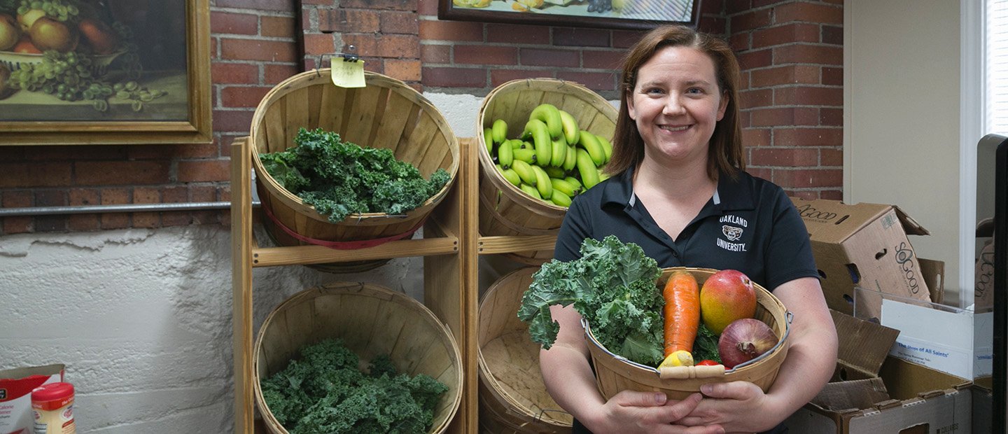 一个女人拿着一篮子蔬菜，前面的架子上放着更多的食物。