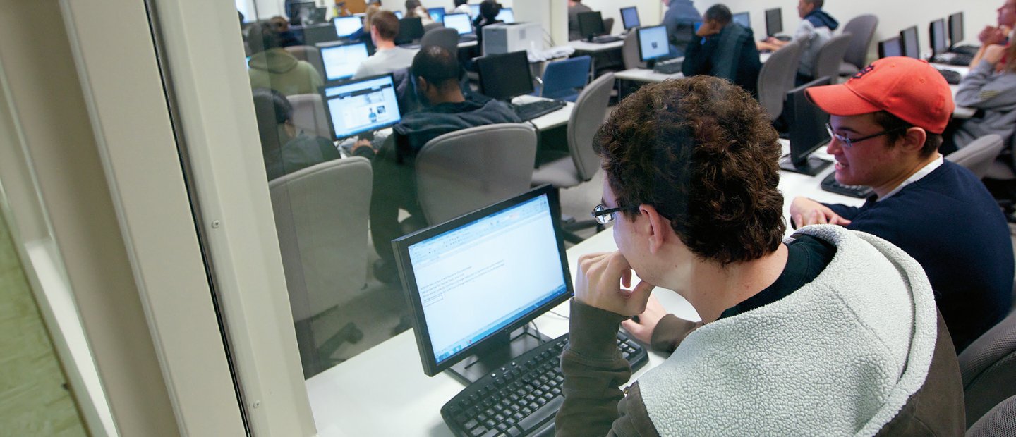 从后面看，学生们坐在有电脑的白色长桌前