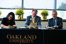三个人坐在一张铺着奥克兰大学桌布的桌子旁，签署官方文件。万博ManBetX登录