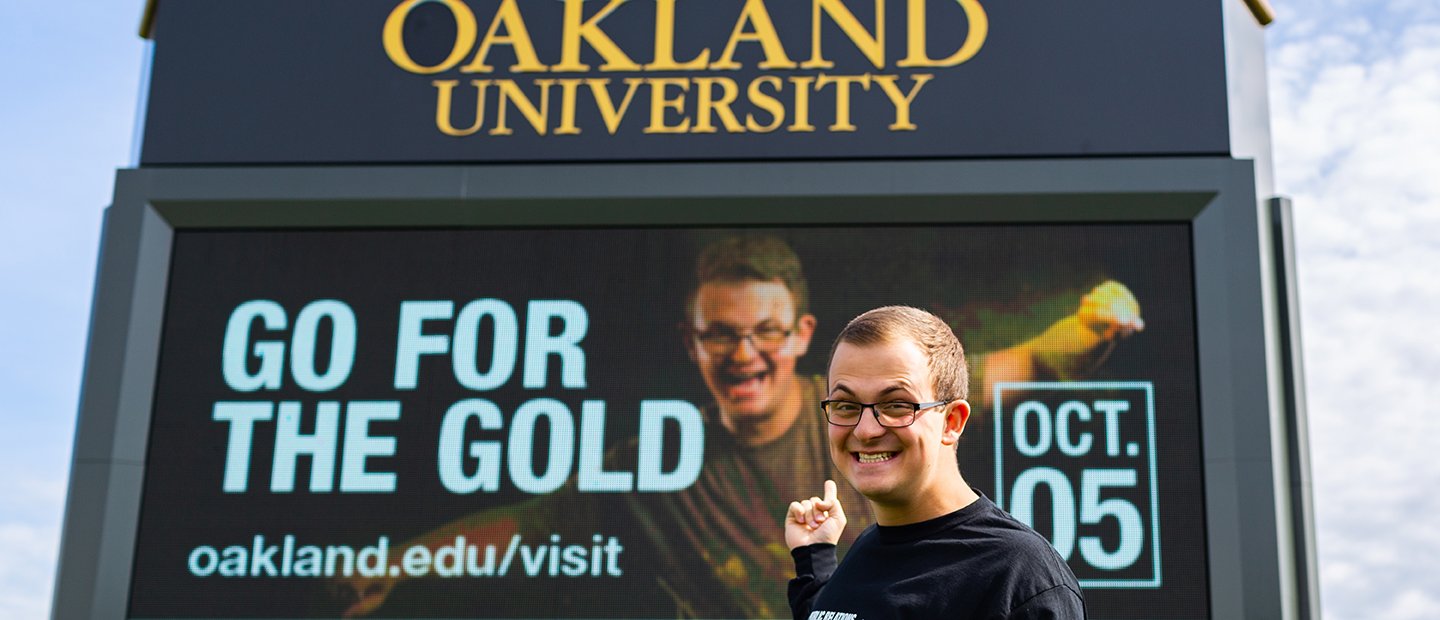 一名年轻男子指着奥克兰大学电子广告牌上的一则广告。万博ManBetX登录
