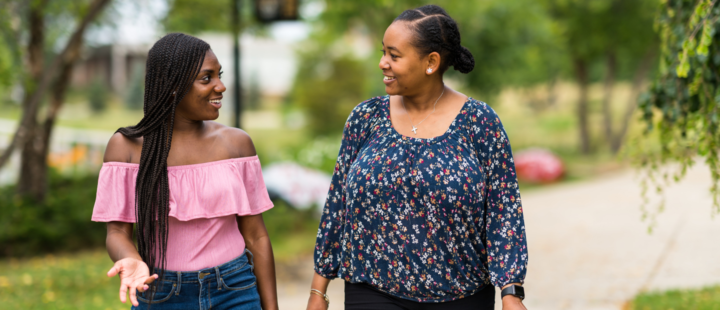 两个女人走在奥克兰大学的校园,微笑和说话。万博ManBetX登录