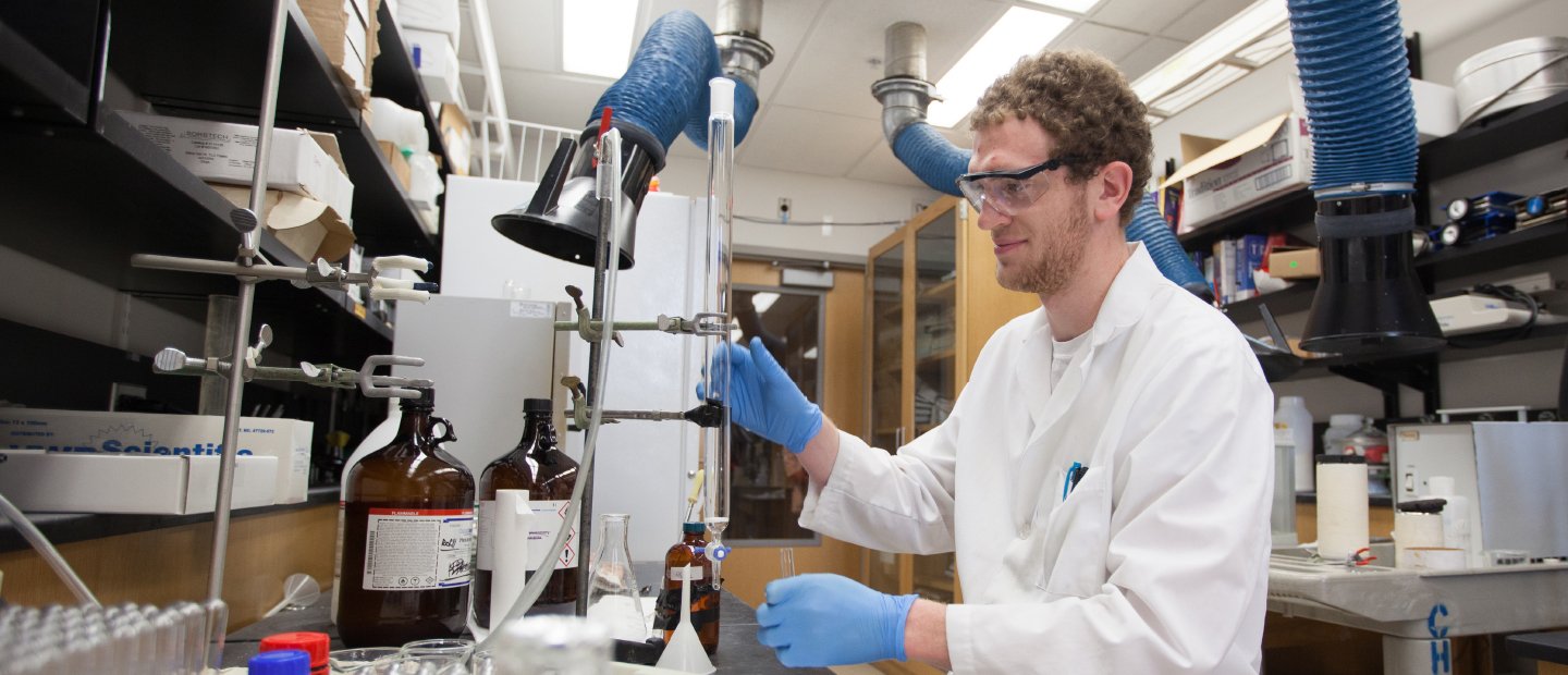 一个穿着白大褂的男人在实验室里用一根长玻璃管处理化学物质。