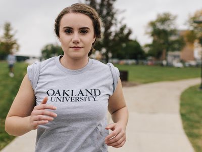 女人穿着奥克兰大学恤,校园慢万博ManBetX登录跑在人行道上
