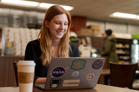 年轻女子坐在咖啡馆喝杯咖啡和一个开放的笔记本电脑。