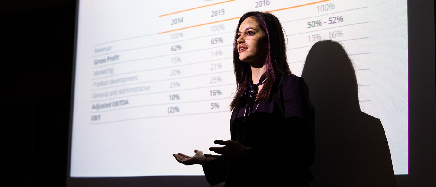 一名年轻女子站在显示百分比数据的投影仪屏幕前。