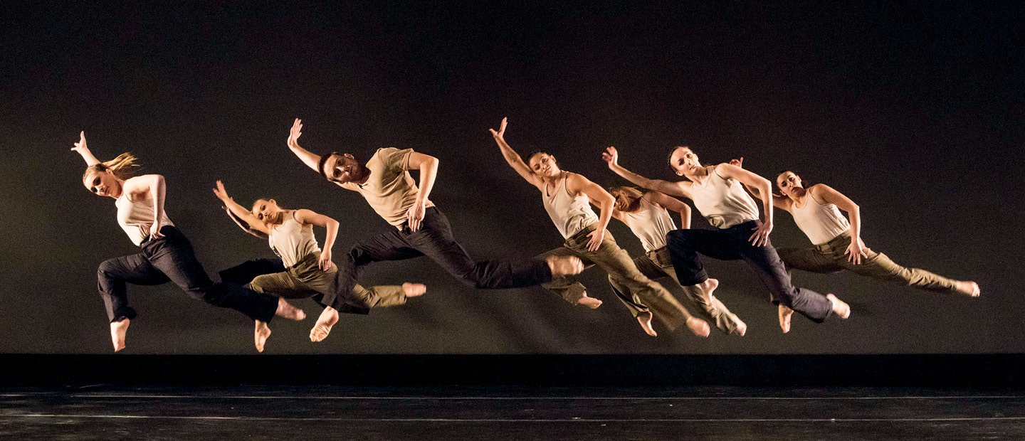 一群舞者都跃入空中，向右倾斜，伸展右臂和左腿。