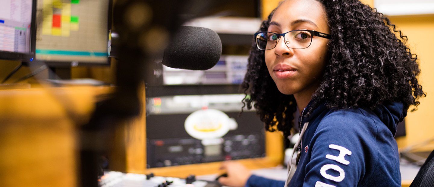 一个学生坐在一个麦克风录音或广播工作室。