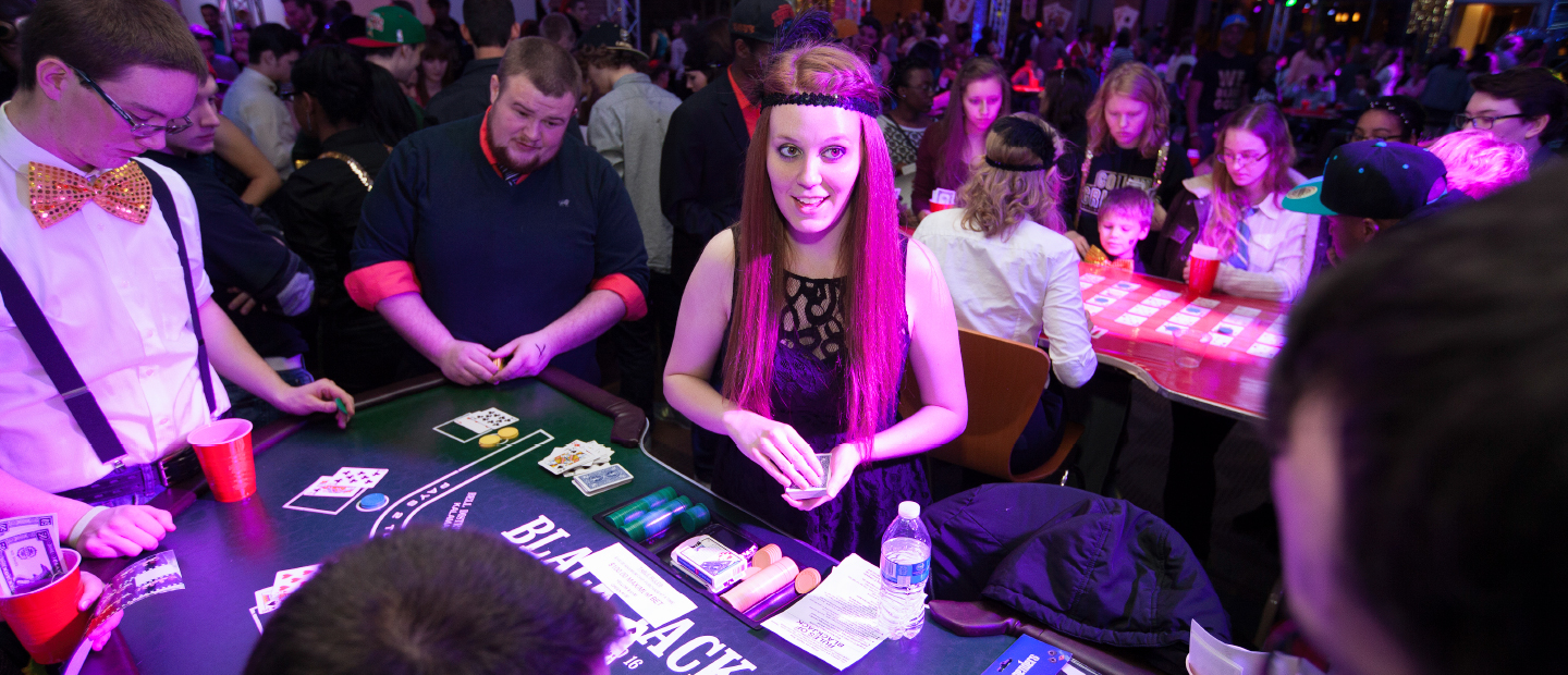 学生计划委员会的网页横幅图片，一个拥挤的房间描绘了一个赌场之夜，以一个女孩打扮成一个扑牌处理卡到桌子
