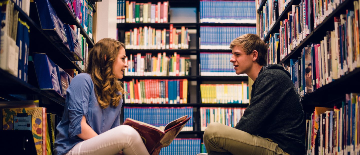 男性和女性学生坐在地板上,阅读,在图书馆