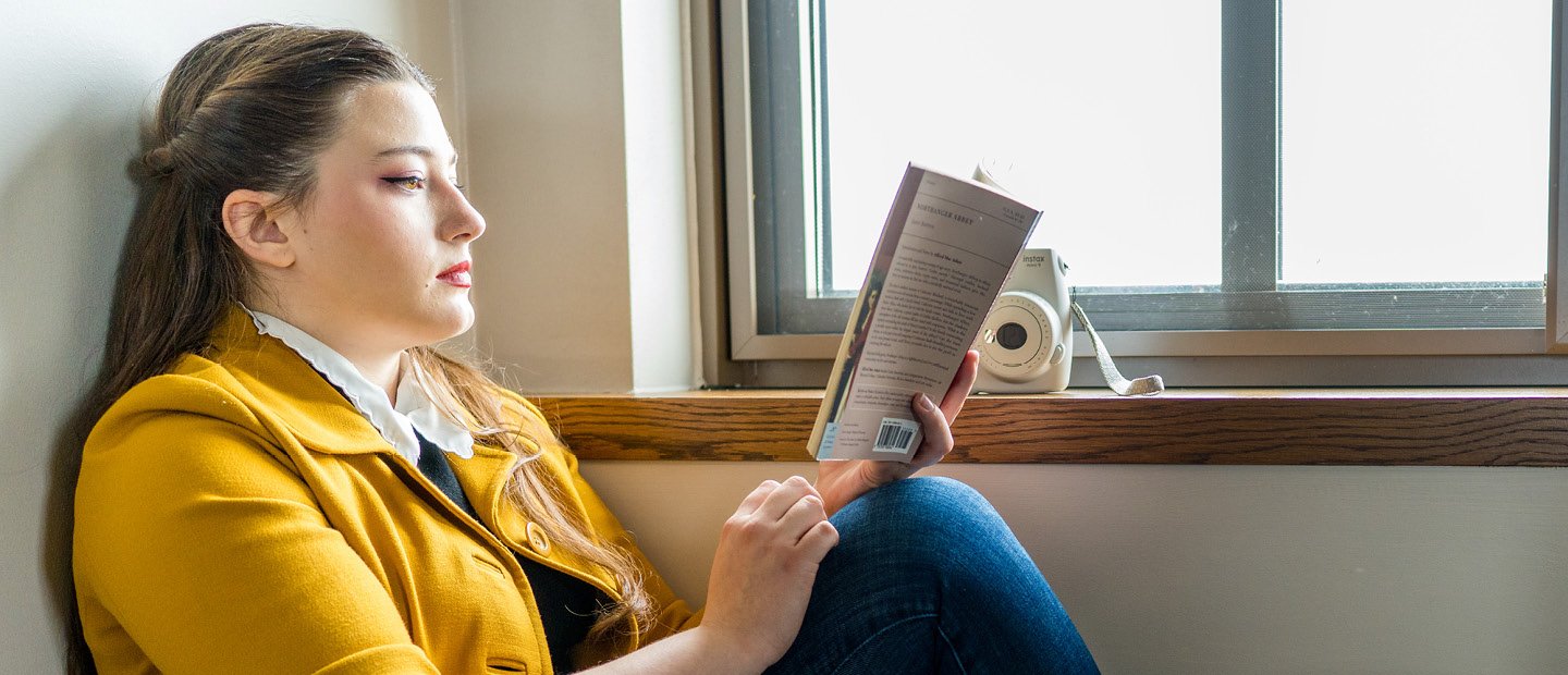 一个女人坐在地板上的一个窗口,看书。
