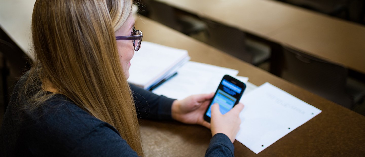 与论文,一个年轻的女人坐在一桌使用智能手机。