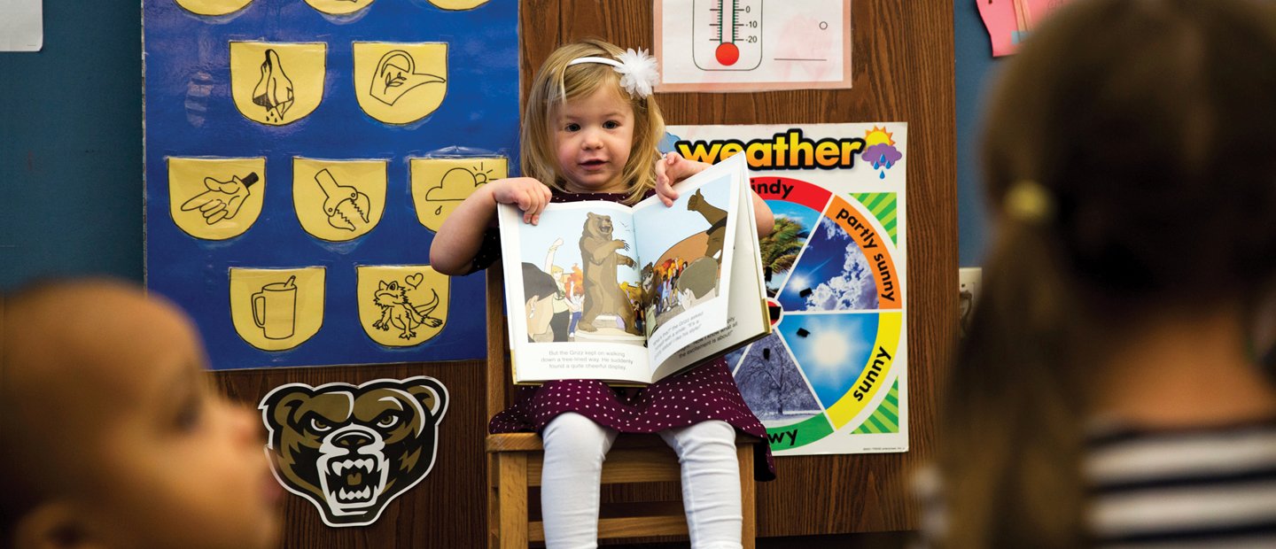 年轻女孩坐在教室前面,显示其他学生一本书。