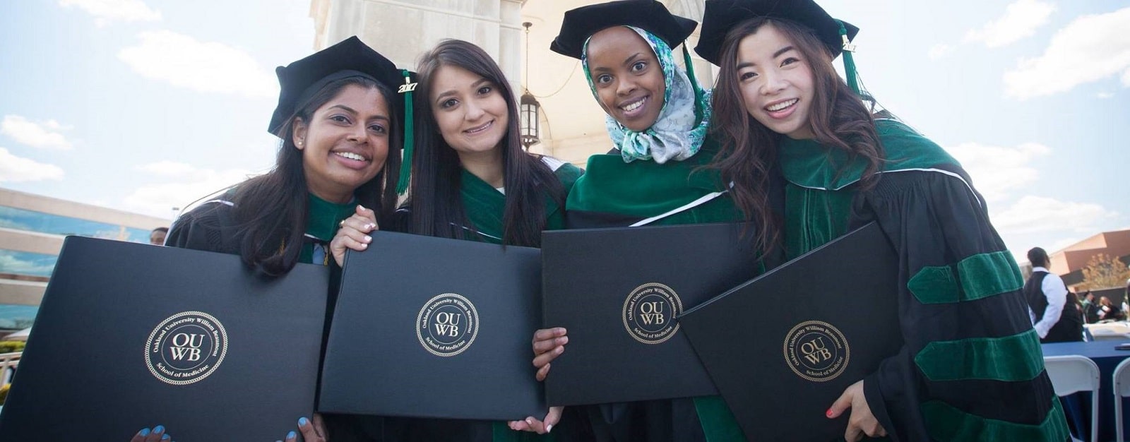 四个新OUWB毕业生站在艾略特塔戴学位帽和学位服,拿着他们的文凭。