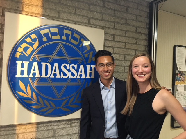 两个学生来到沙龙站立,微笑,面对一大斑块Hadassah医学中心的标志。