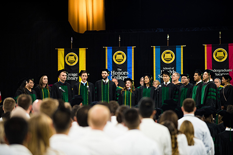2018届U O W B DocAppella唱诗班的成员在舞台上唱歌的彩色的旗帜在毕业典礼