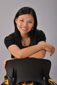 一个穿黑衬衫的女人，靠在椅背上，对着镜头微笑