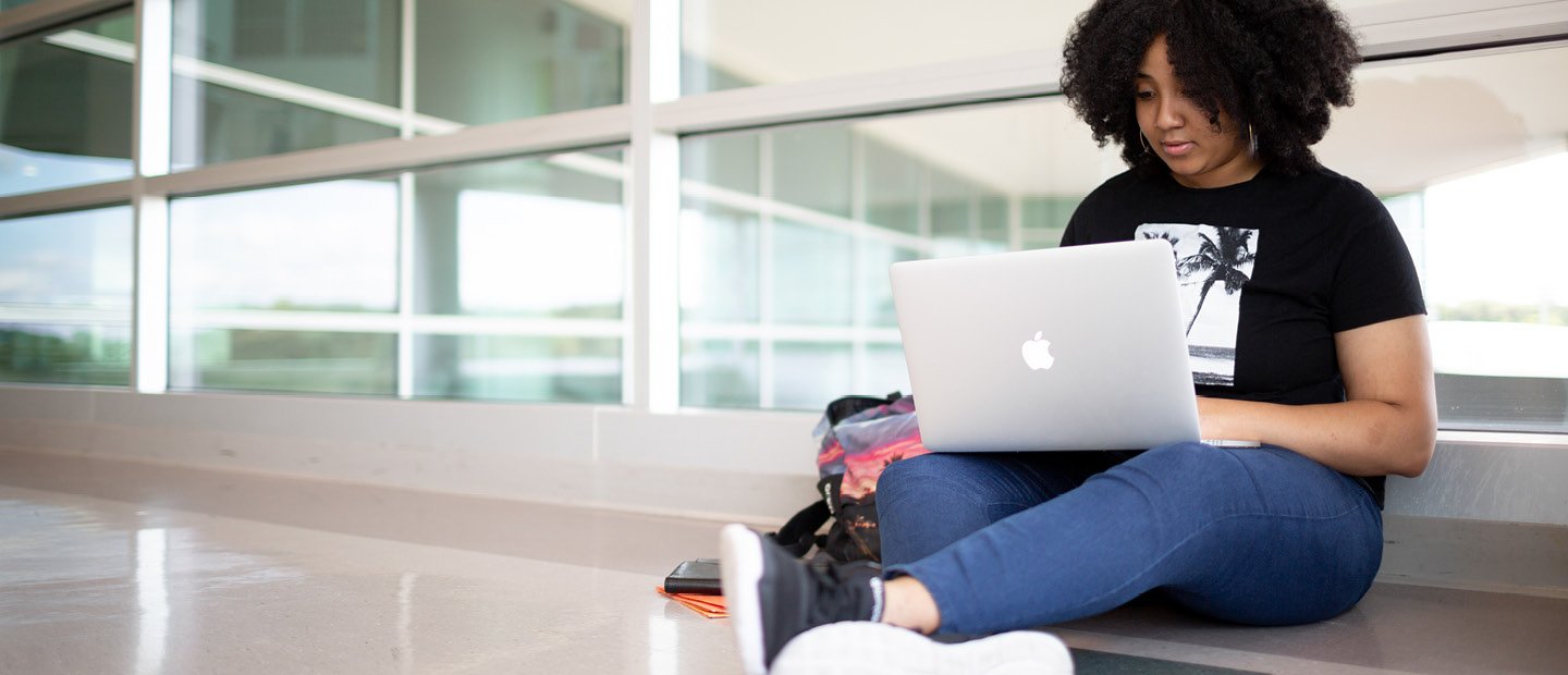 年轻女子坐在前面的地板上一个窗口和一个开放的笔记本电脑在她的大腿上