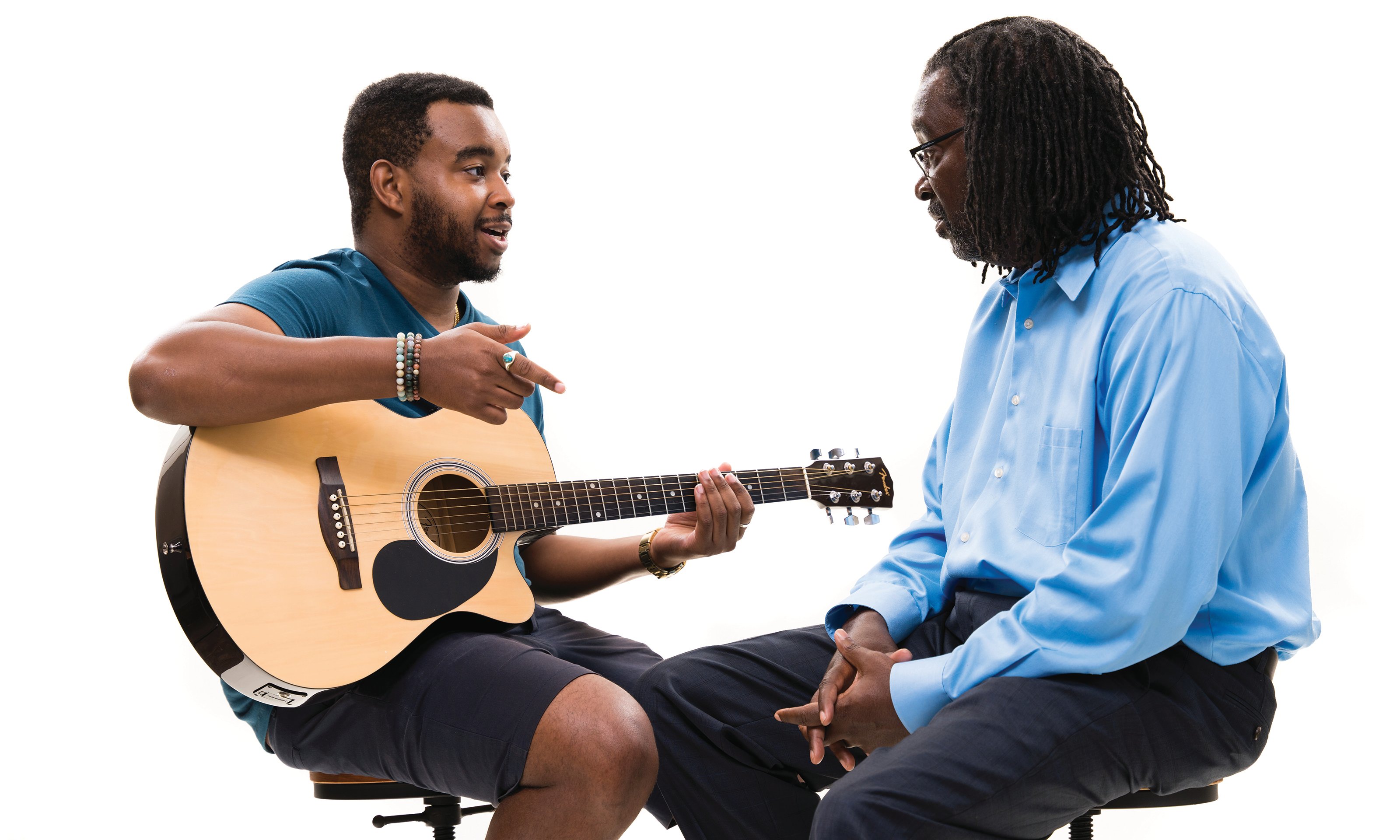 一个人坐着，拿着吉他和另一个人说话。
