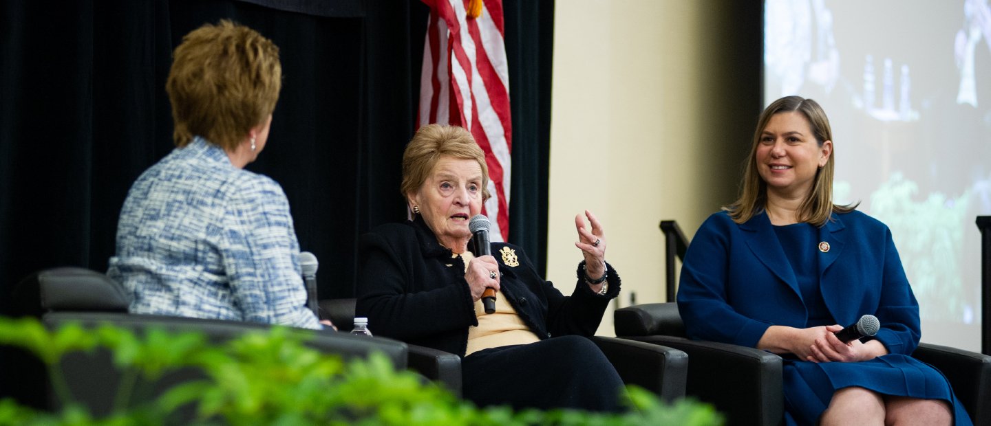 三位女性政客们坐在舞台前面一个投影仪。一个是对麦克风讲话。