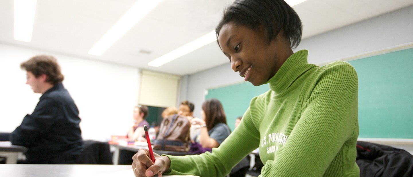 一名年轻女子坐在教室的书桌前，在笔记本上写字。