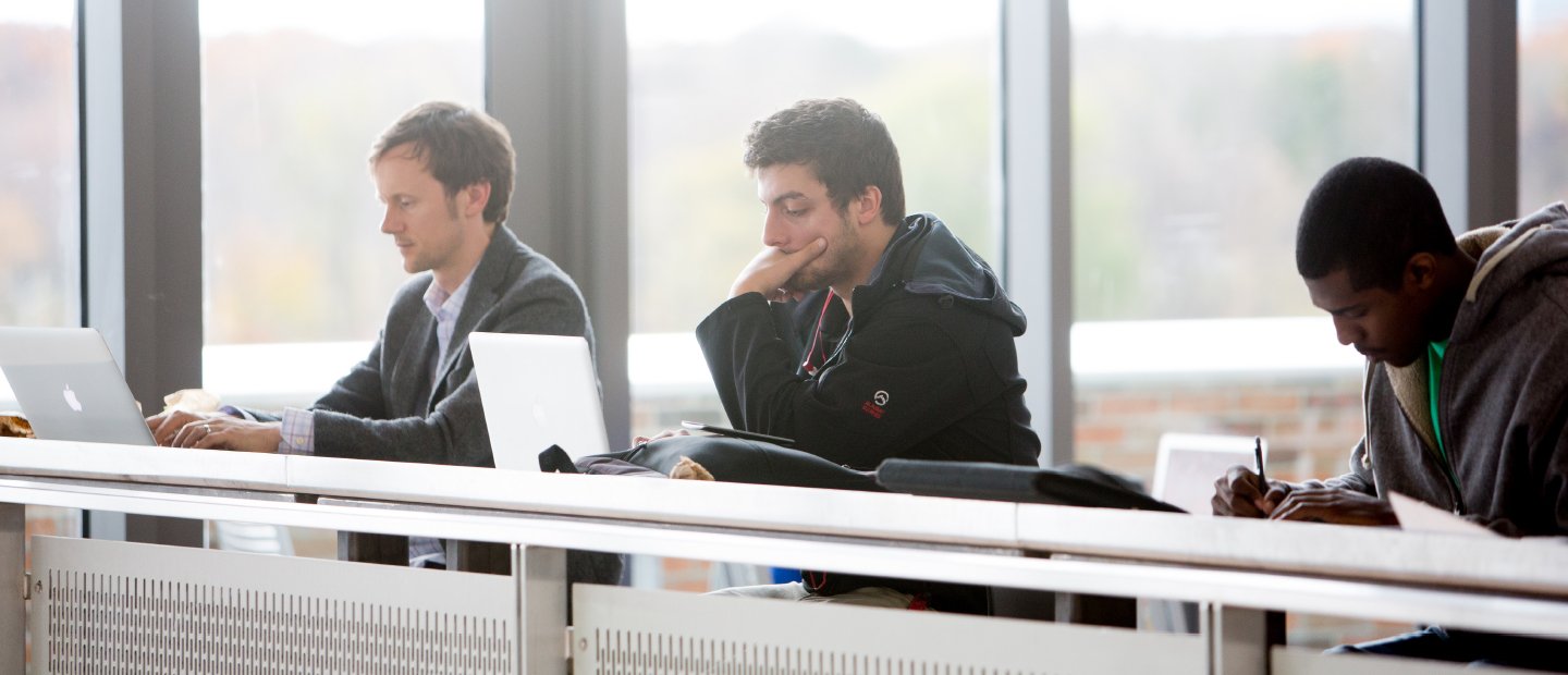 三个学生用笔记本电脑坐在长桌子