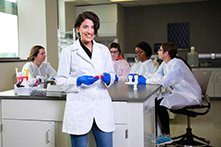 Arwa哈迪德穿白大褂的和蓝色的手套在临床实验室和诊断科学与其他学生坐在她身后。