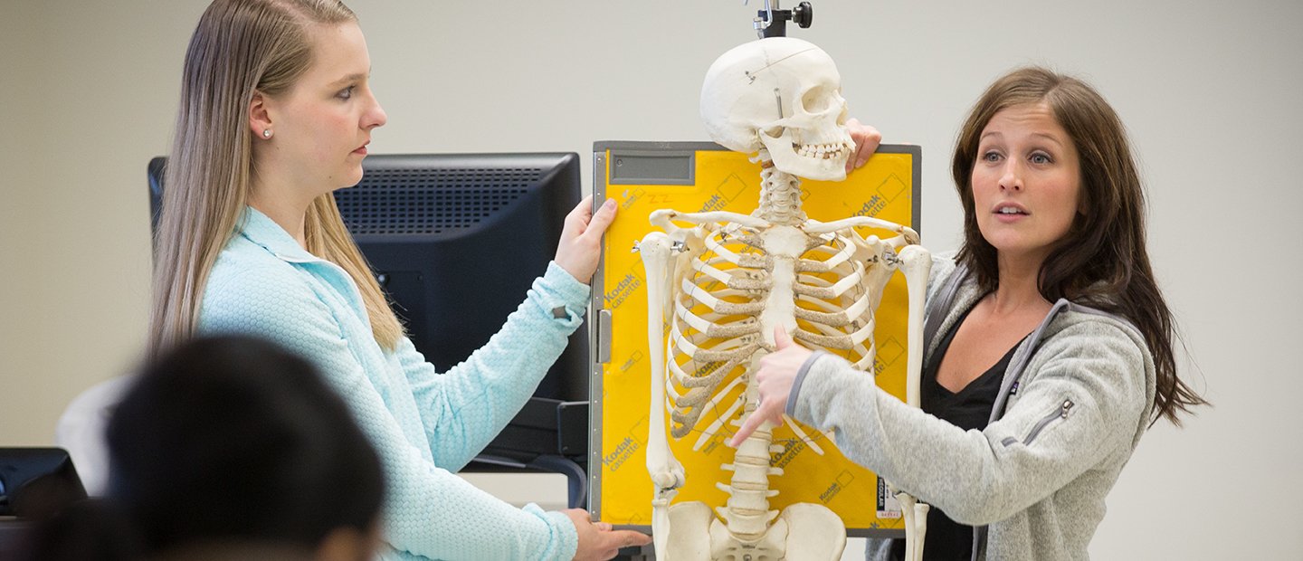 两名妇女举着骨架模型站在教室前