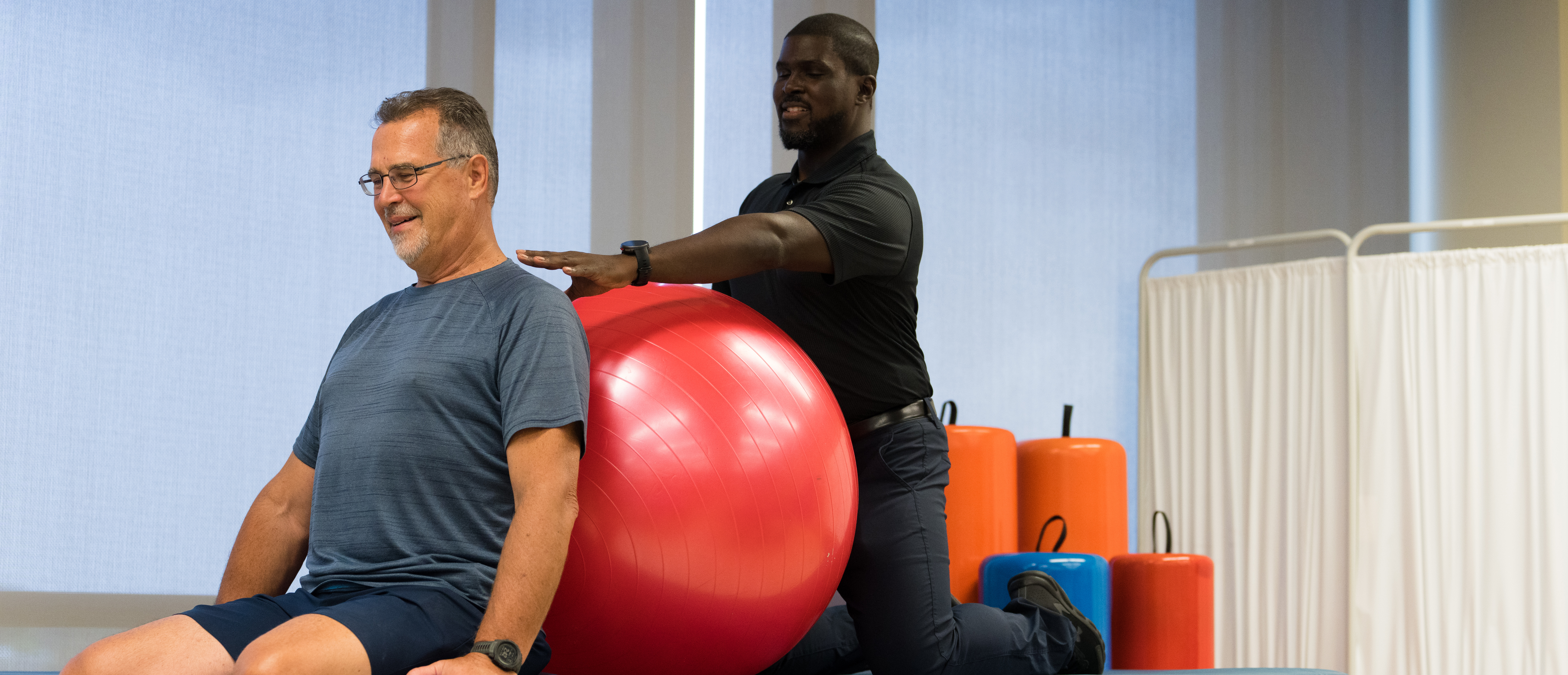 男性的物理治疗师帮助一个男人与一个练习球在一个健身工作室。