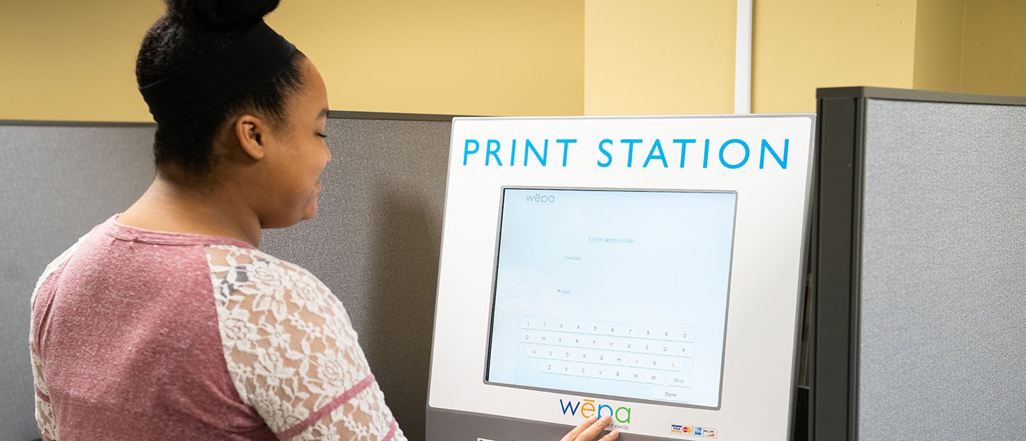 一个年轻的女人站在打印站的电脑屏幕前