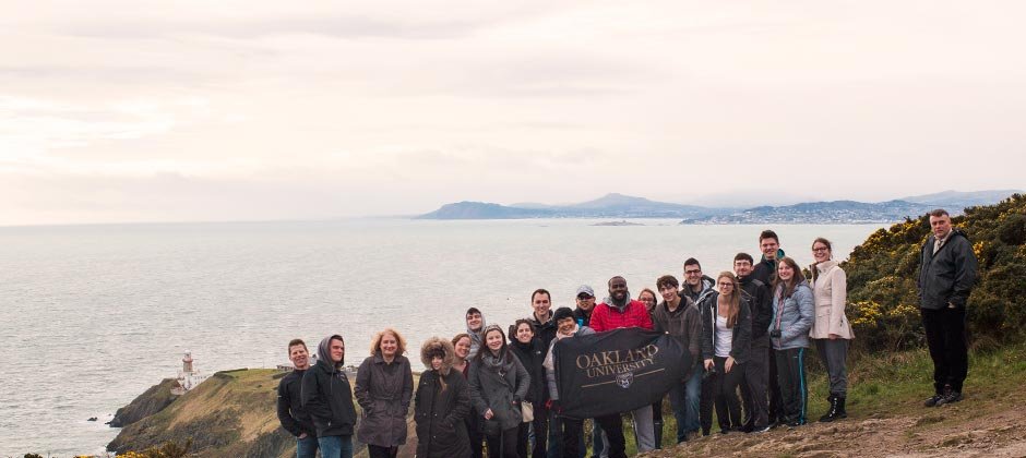 一群在国外学习的欧大学生举着欧大的横幅站在大海前